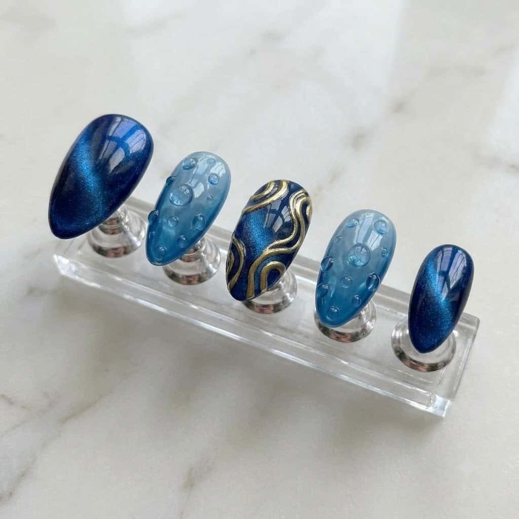 Five blue cat eye nails on a clear acrylic stand