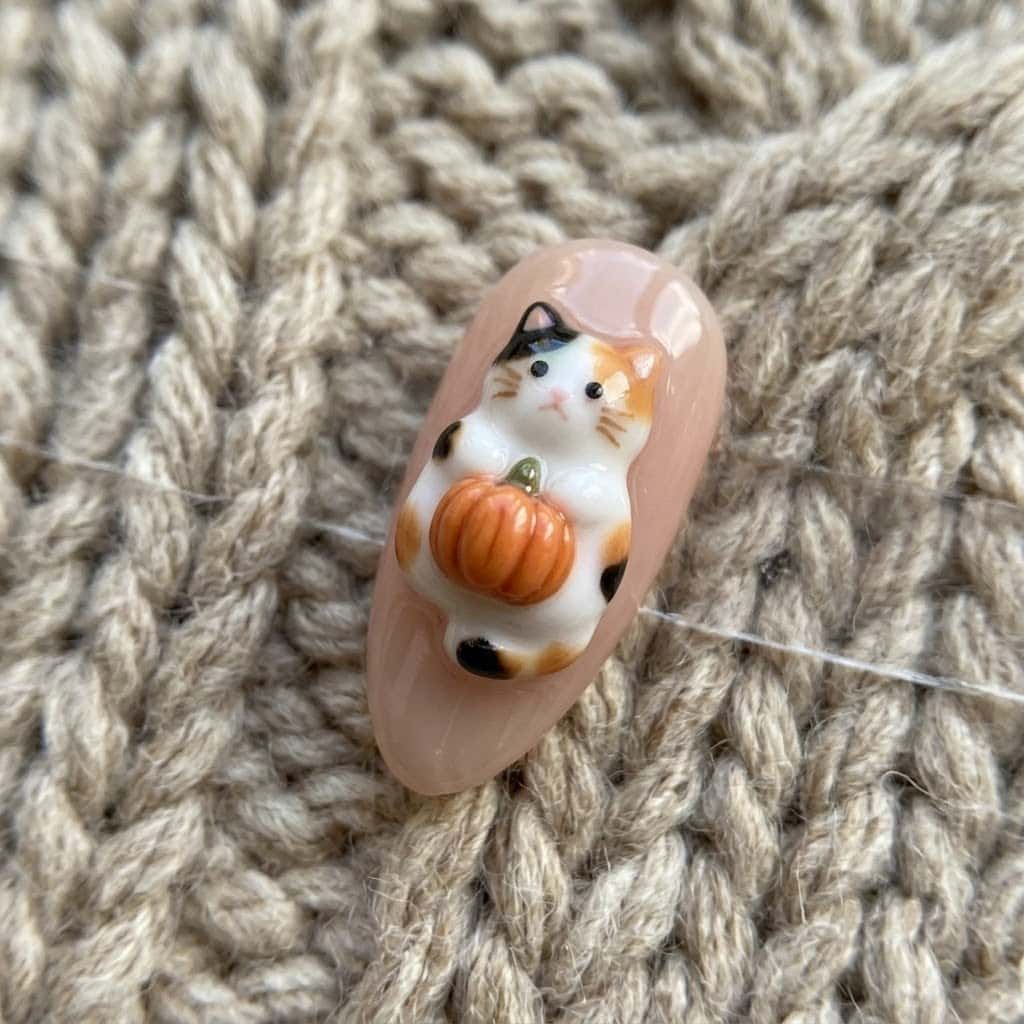 Close-up of the raised 3D calico cat hugging a tiny orange pumpkin