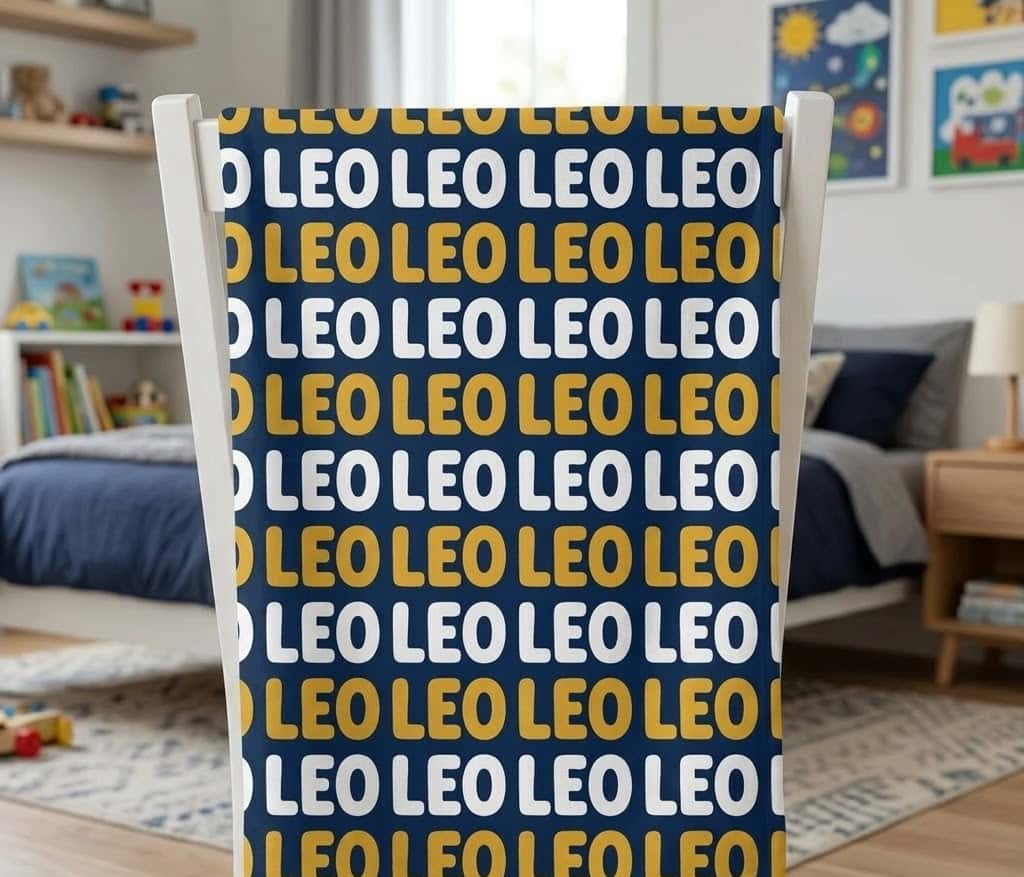 Leo navy repeat name blanket hung flat over a white chair back