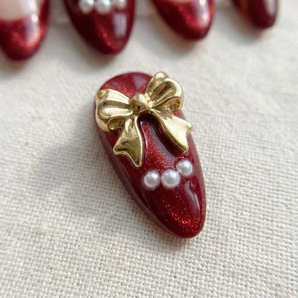 Close-up of ruby cat eye nail with 3D gold bow and pearls