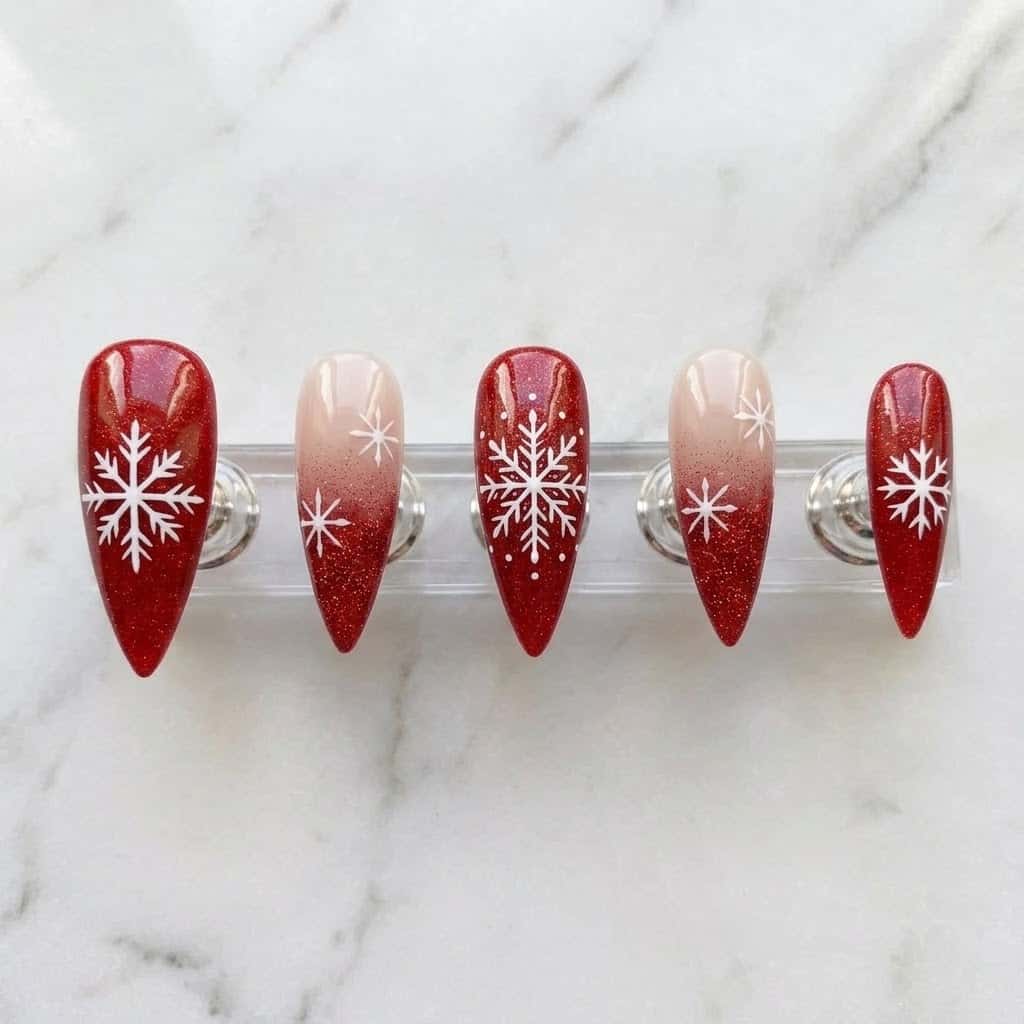 Five red snowflake stiletto nails on a clear acrylic stand