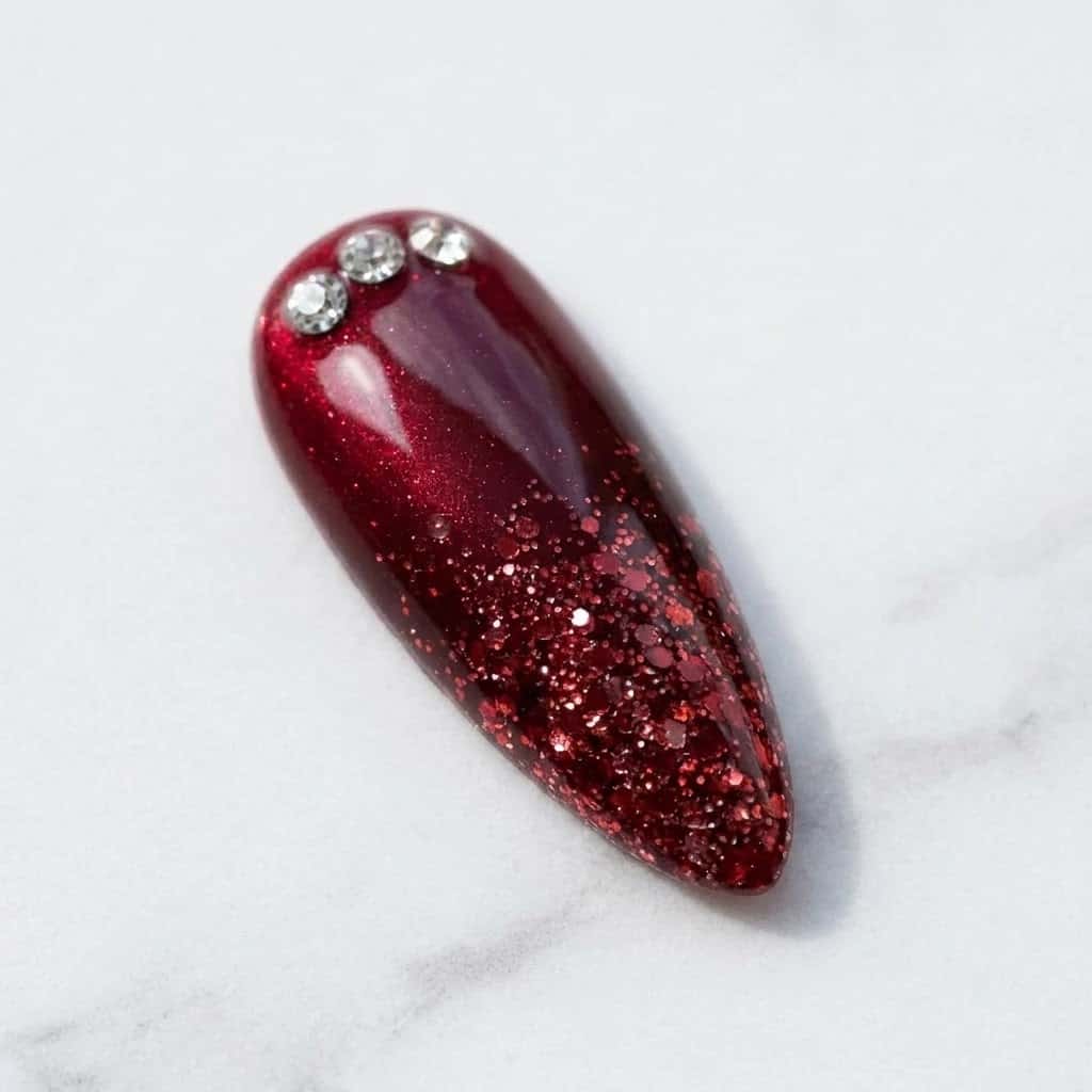 Close-up of red cat eye nail with ruby glitter ombre and crystals