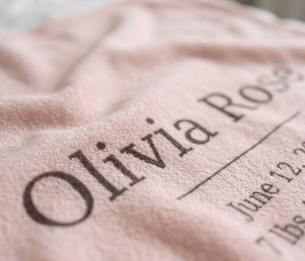 Close-up of serif Olivia Rose name and birth date on blush flannel