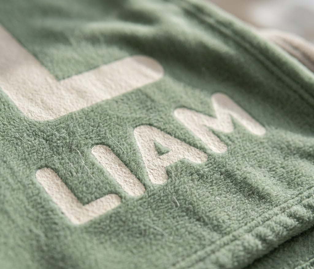Close-up of the cream L and Liam lettering on soft sage flannel