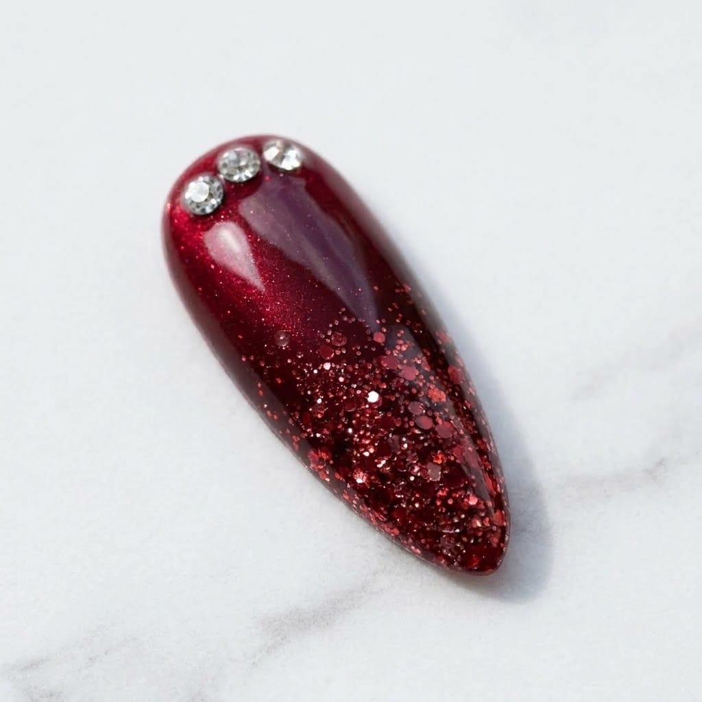 Close-up of red cat eye nail with ruby glitter ombre and crystals